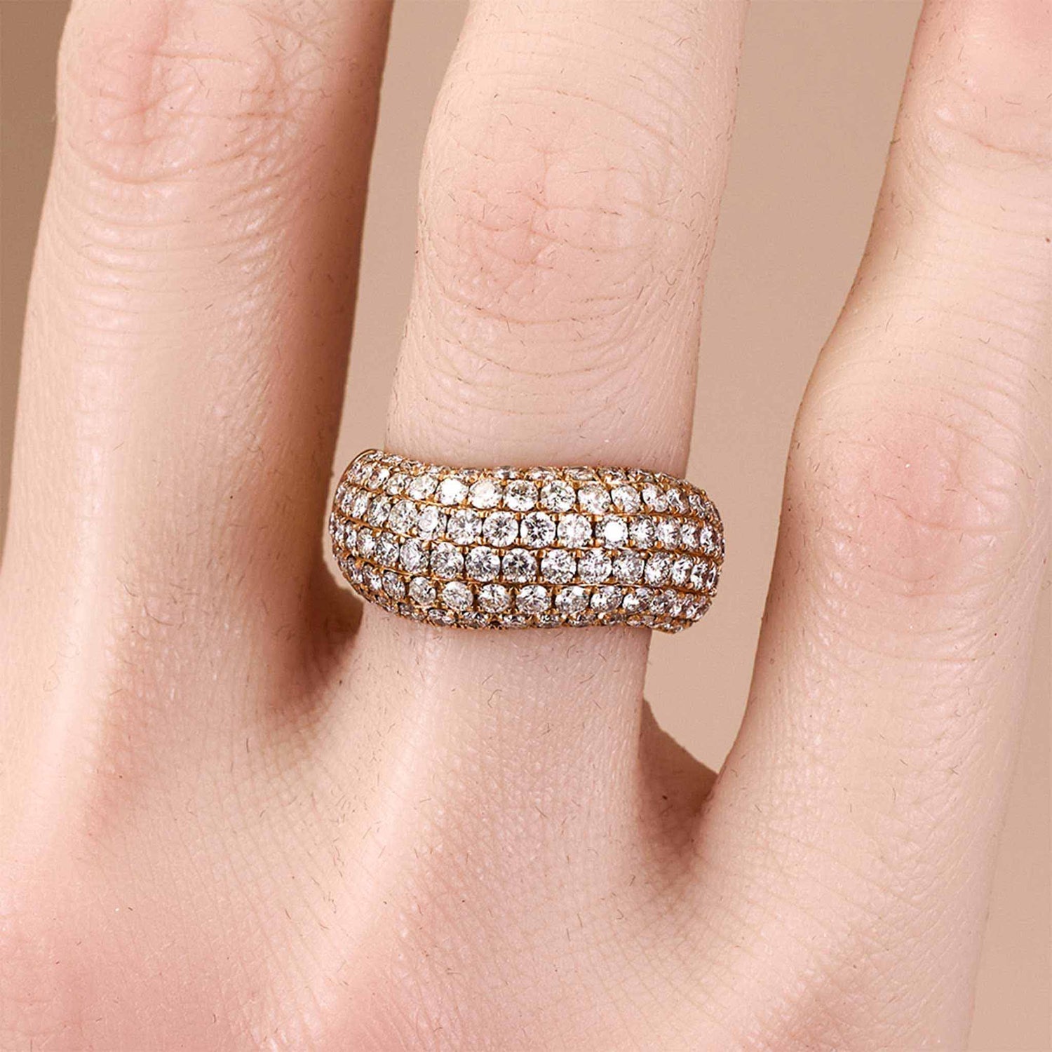 Rose gold ring with diamonds on a finger against a beige background from JewelryandStore